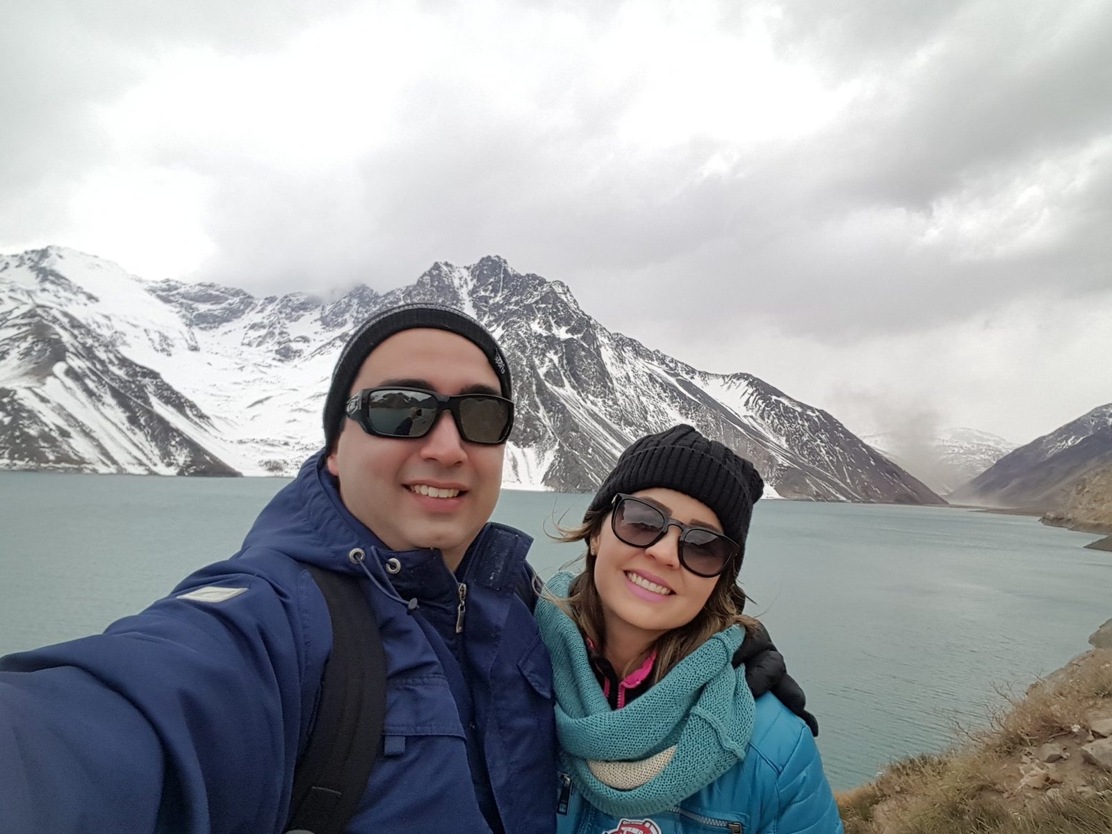 Selfie diante de um lago entre montanhas nevadas